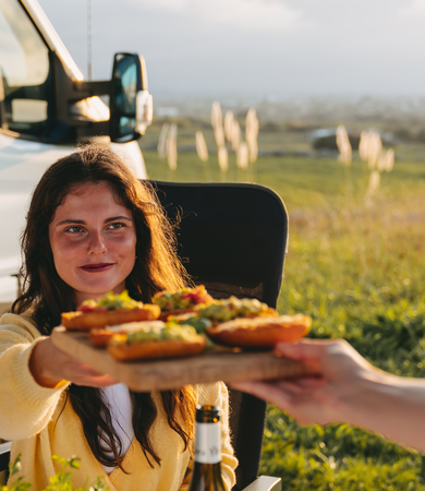A woman sits in front of an Etrusco semi-integrated motorhome on a Ford base and serves avocado toast.
