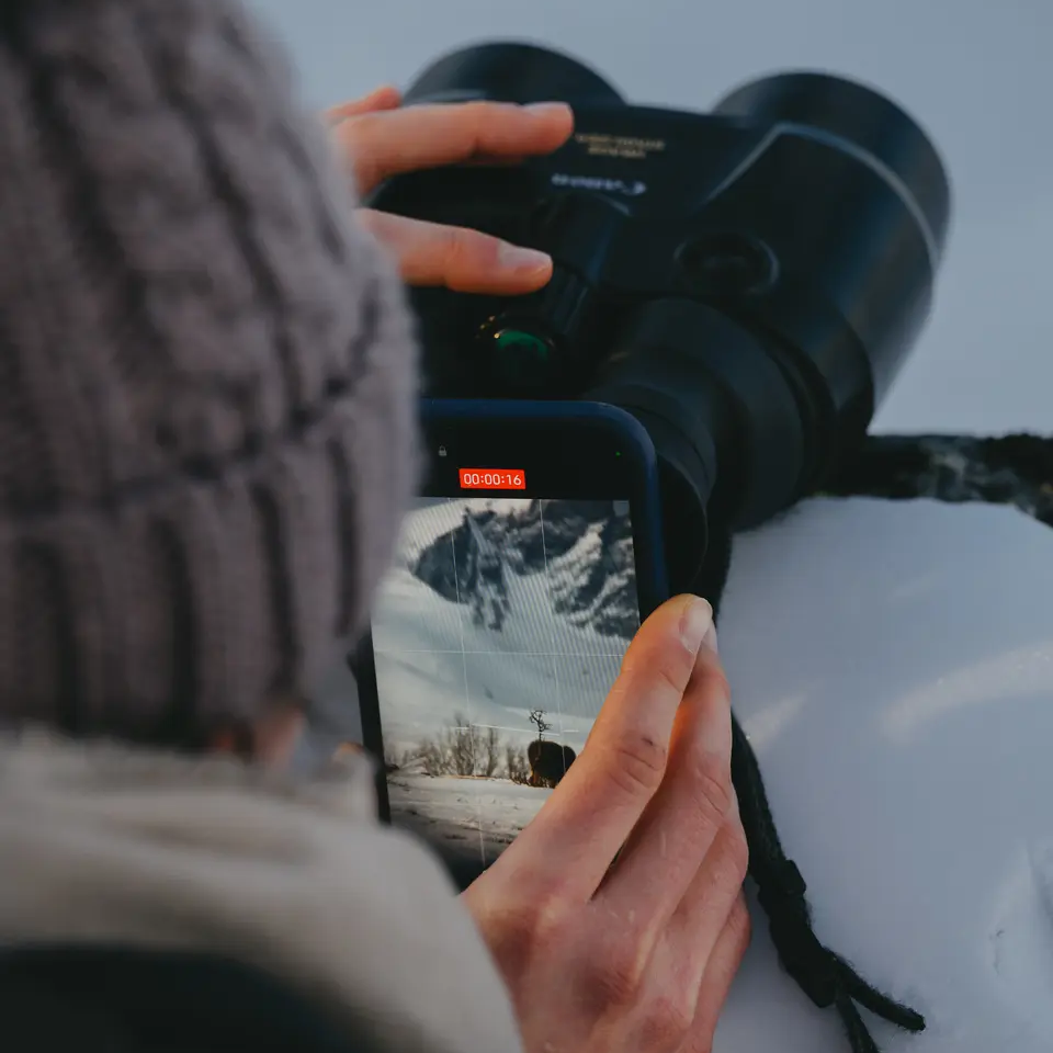 Kvinne filmer med telefonen sin gjennom en kikkert